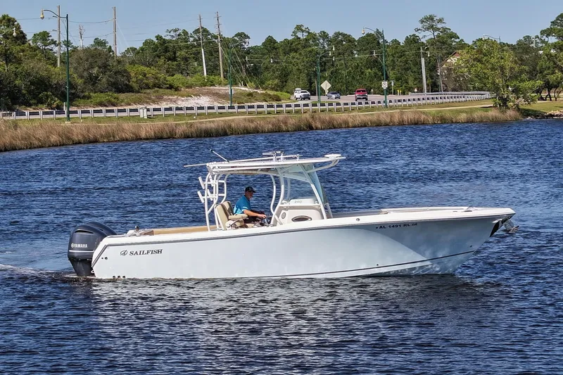 Slide: The Image of 2018 Sailfish 290 CC boat cruising on a calm river with lush greenery in the background. - 9
