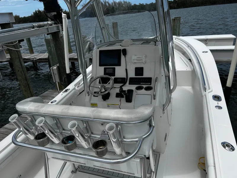 Slide: The Image of 2018 Regulator 23 Forward Seating boat with helm, rod holders, and electronics, docked by the water. - 18