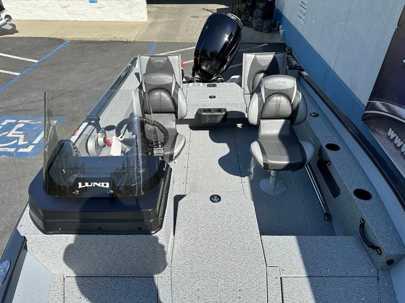 Slide: The Image of 2025 Lund 1675 Adventure SS boat interior with seating and controls, parked outdoors. - 25