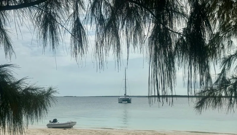 Slide: The Image of Sailboat anchored near beach, framed by trees, with inflatable dinghy on shore. - 37