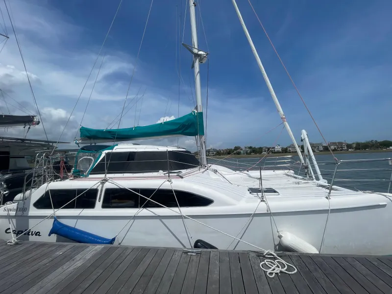 Slide: The Image of 2001 Seawind 1000 catamaran docked, featuring white hull and teal sail, under clear sky. - 3