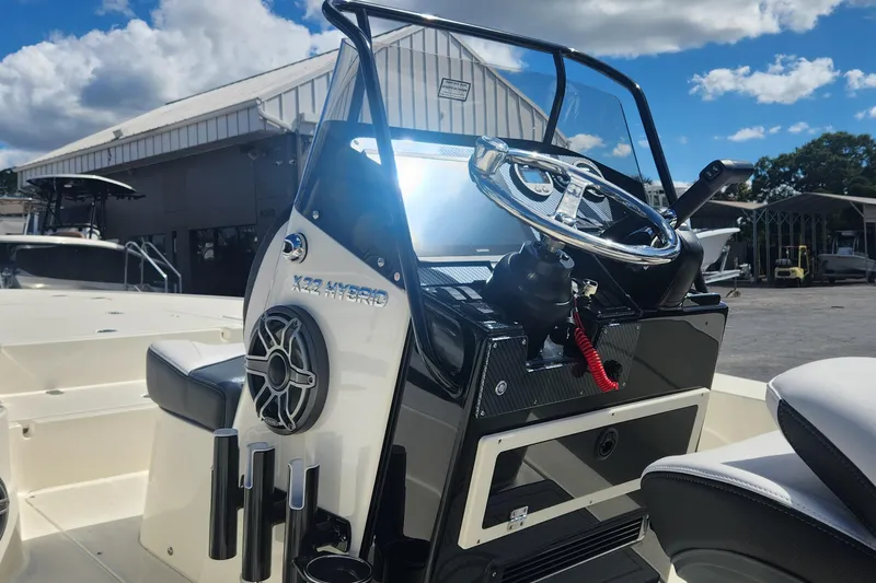 Slide: The Image of 2026 ShearWater X22 HYBRID boat console with steering wheel and speaker, under sunny skies. - 10