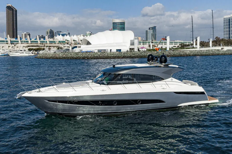 Slide: The Image of 2023 Riviera 5400 Sport Yacht cruising in a marina with city skyline backdrop. - 0