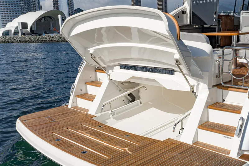Slide: The Image of 2023 Riviera 5400 Sport Yacht with open storage compartment, docked near modern architecture. - 17