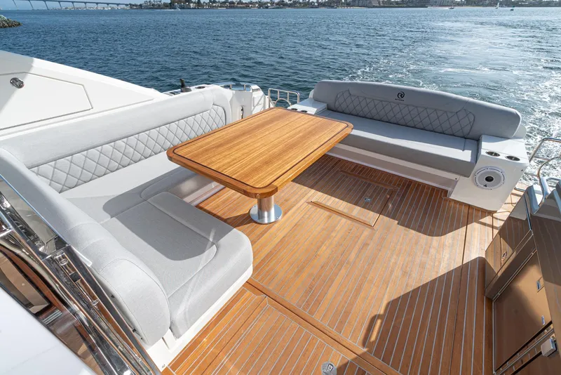 Slide: The Image of 2023 Riviera 5400 Sport Yacht deck with elegant seating and wooden table, overlooking serene waters. - 23