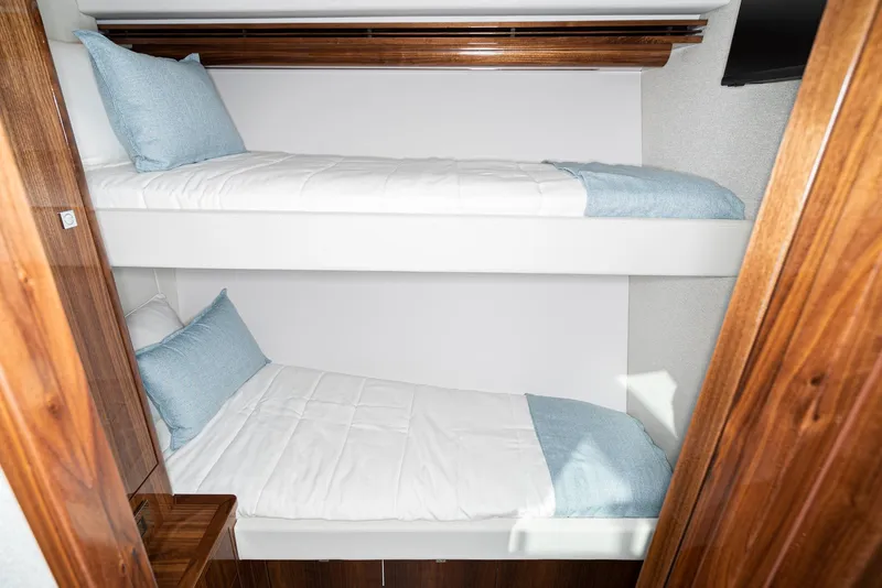 Slide: The Image of 2023 Riviera 5400 Sport Yacht interior with cozy bunk beds and wooden accents. - 47