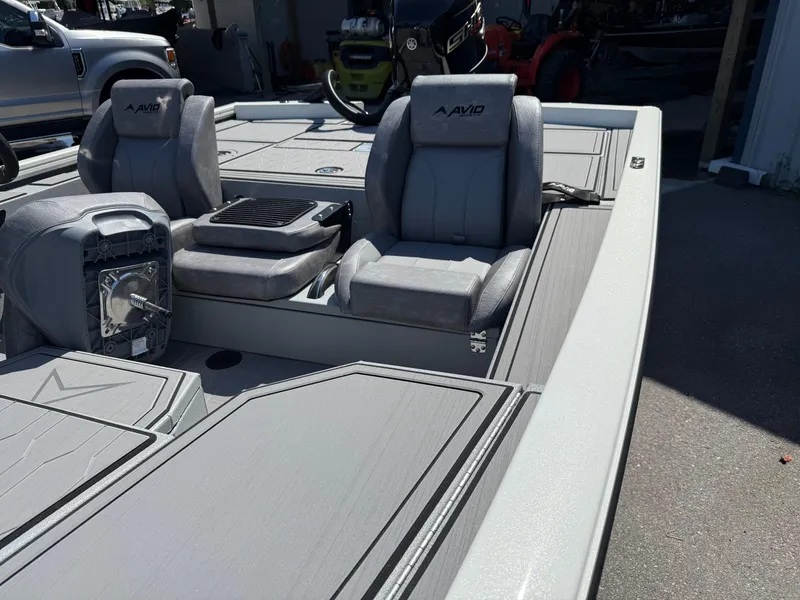 Slide: The Image of 2025 Avid 18 XB boat interior with gray seating and deck, parked outdoors. - 7