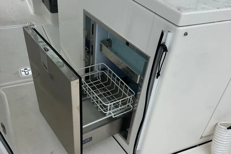 Slide: The Image of Open storage compartment on a 2019 Pursuit DC 325 boat, featuring a wire basket. - 20