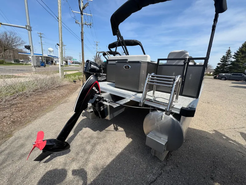 Slide: The Image of 2025 Qwest E 20 Lanai pontoon boat with outboard motor, parked on pavement. - 5
