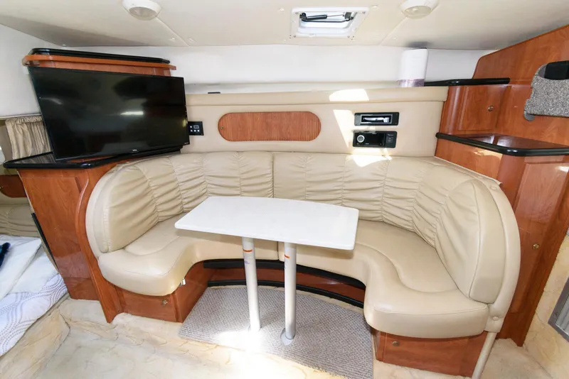 Slide: The Image of 2004 Rinker Fiesta Vee 312 interior with beige leather seating, table, and mounted TV. - 18