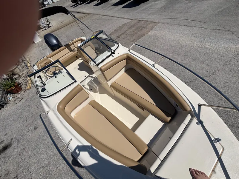 Slide: The Image of 2018 Scout 210 Dorado boat with beige seating and dual consoles, parked on pavement. - 46