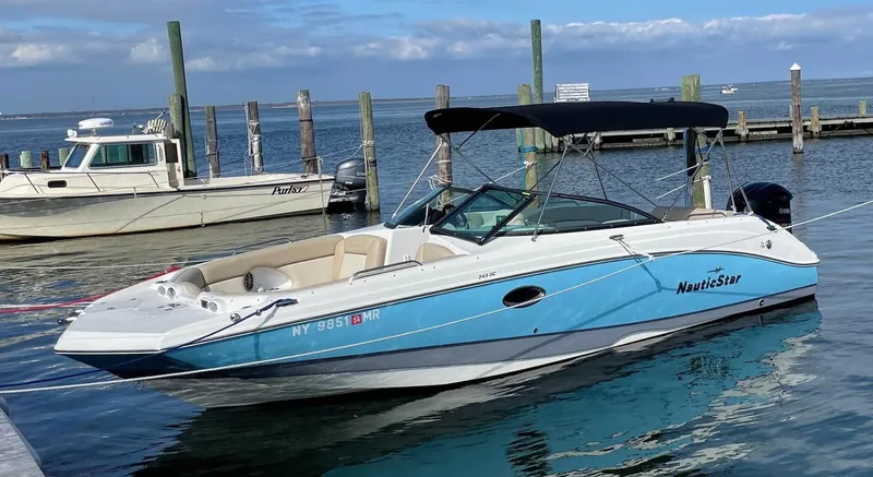 Slide: The Image of 2021 NauticStar 243 DC boat docked in a marina, featuring a sleek blue and white design. - 1