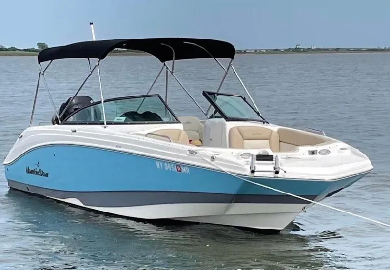 Slide: The Image of 2021 NauticStar 243 DC boat with blue hull, anchored on calm water. - 2