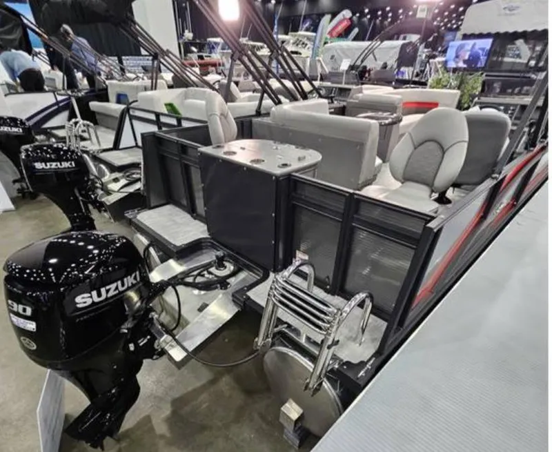 Slide: The Image of 2025 Qwest E 20XRE pontoon boat with Suzuki outboard motor, showcased indoors. - 2