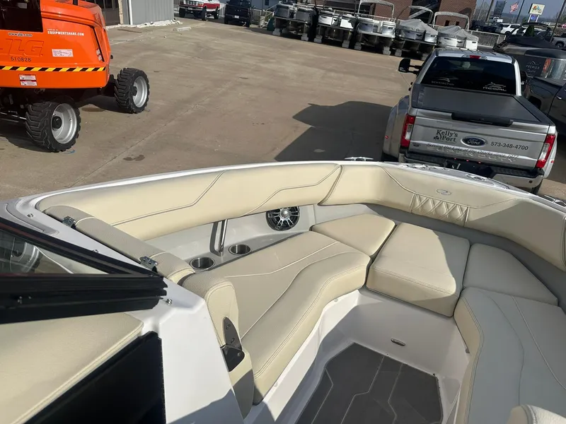 Slide: The Image of 2022 Regal LS4 Surf boat with beige seating, parked near a truck and construction equipment. - 11