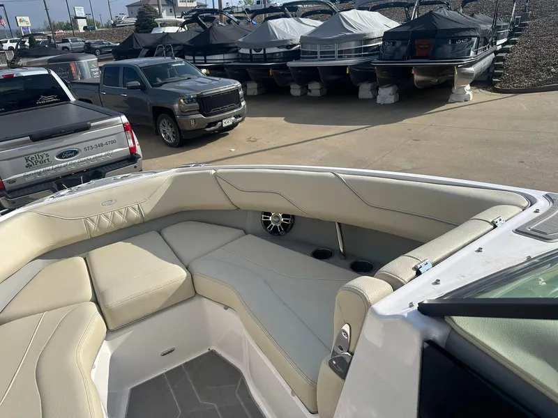 Slide: The Image of 2022 Regal LS4 Surf boat interior with beige seating, parked near trucks and covered boats. - 9