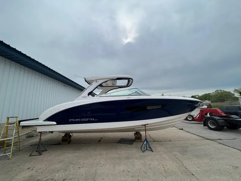 Slide: The Image of 2025 Regal 3300 boat on stands, blue and white hull, overcast sky background. - 1