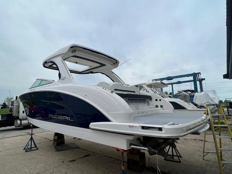 Slide: The Image of 2025 Regal 3300 boat on stands, sleek design, white and blue exterior. - 2