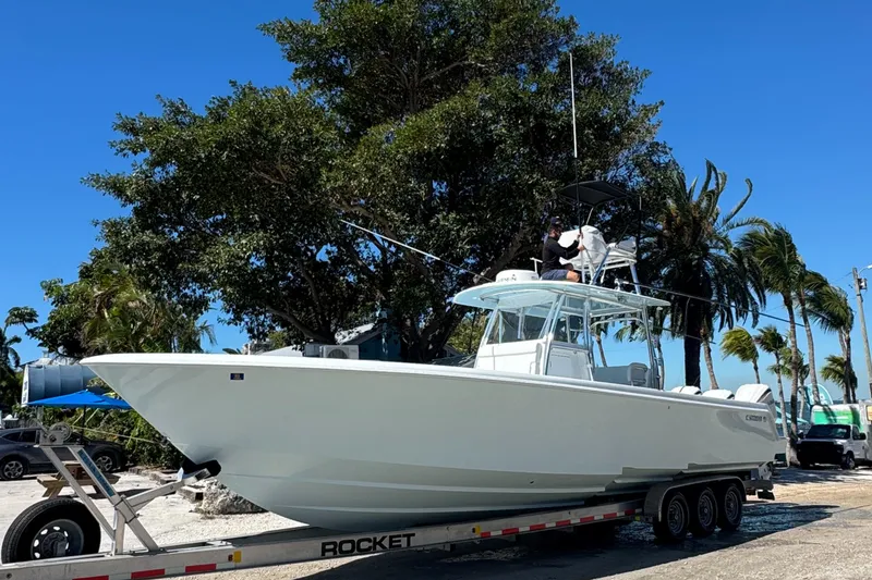 Slide: The Image of 2024 Contender 39 ST boat on trailer, parked under trees, clear blue sky. - 1