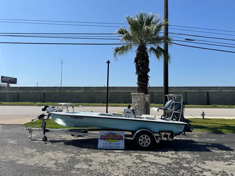 Slide: The Image of 2023 Hell's Bay Professional boat on trailer, parked near a palm tree under clear blue sky. - 1