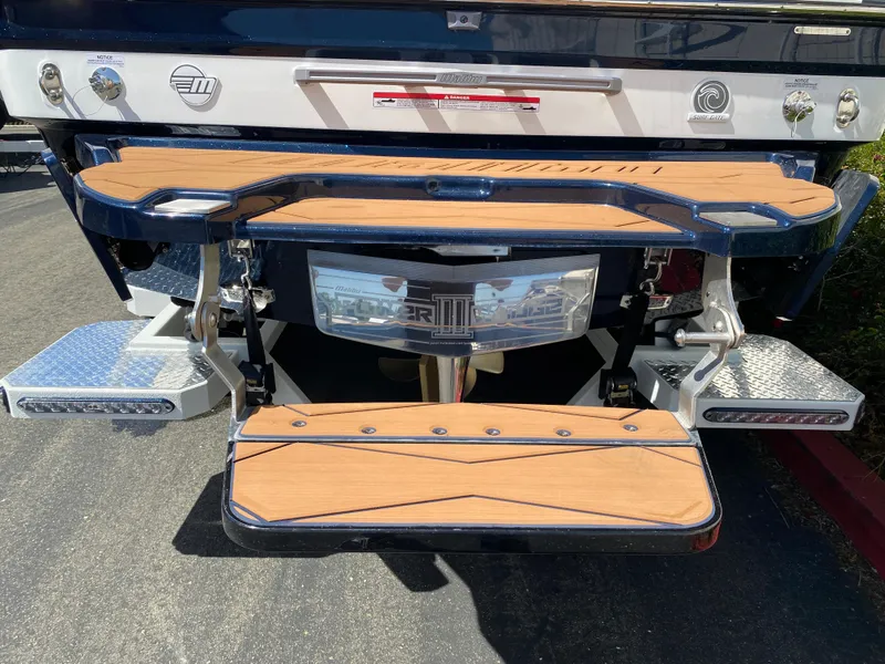 Slide: The Image of 2025 Malibu Wakesetter 24 MXZ boat stern with teak swim platform and chrome accents. - 6