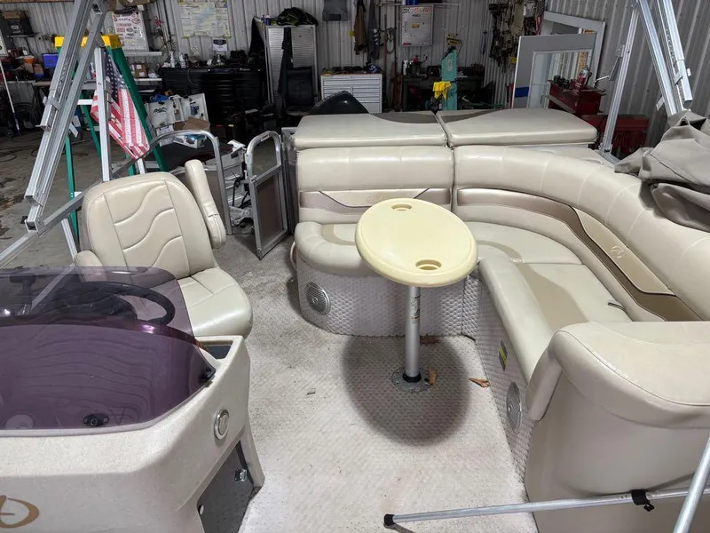 Slide: The Image of 2011 Avalon LS 23' RE pontoon boat interior with beige seating and table in a workshop. - 12