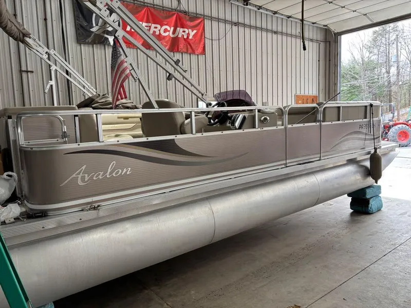 Slide: The Image of 2011 Avalon LS 23' RE pontoon boat in a garage with Mercury banner. - 16