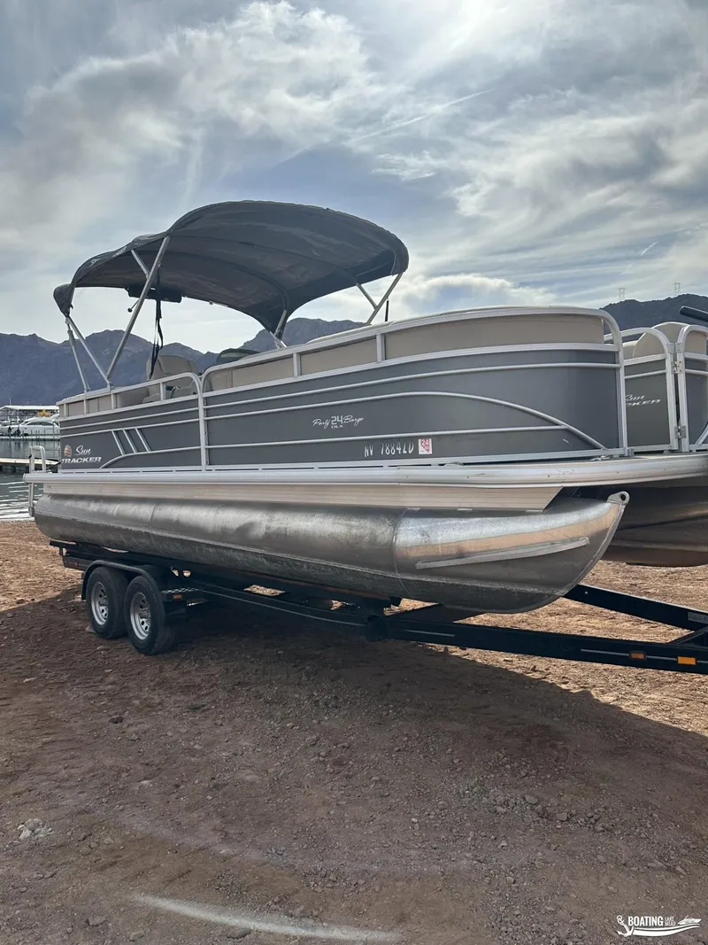 Slide: The Image of 2020 Tracker Party Barge 24 DLX pontoon boat on trailer, under cloudy sky. - 2