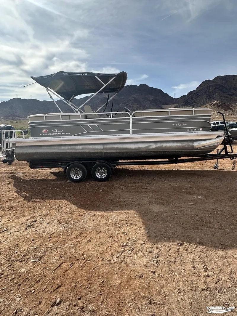 Slide: The Image of 2020 Tracker Party Barge 24 DLX pontoon boat on trailer, parked on dirt with mountains in background. - 4