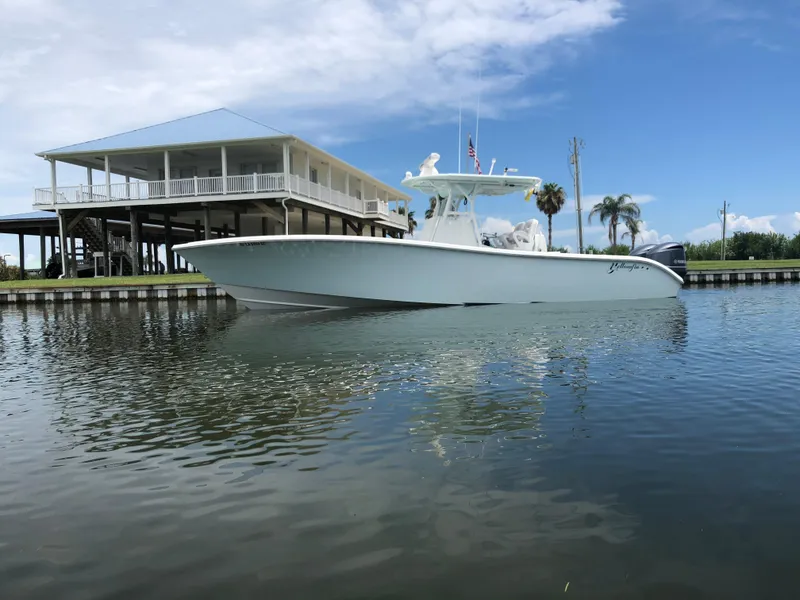 Slide: The Image of 2014 Yellowfin 32 Offshore boat on calm water near a waterfront house. - 0
