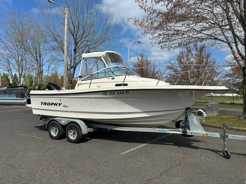 Slide: The Image of 2002 Trophy Pro boat on trailer in parking lot, surrounded by trees and blue sky. - 1