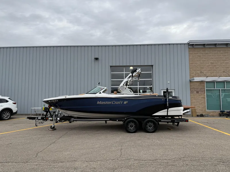 Slide: The Image of 2018 MasterCraft XT23 boat on trailer, parked outside industrial building. - 1