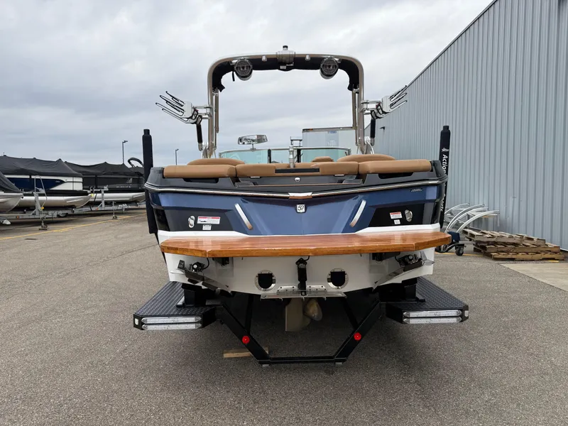 Slide: The Image of 2018 MasterCraft XT23 boat, rear view, parked outdoors near a metal building. - 4
