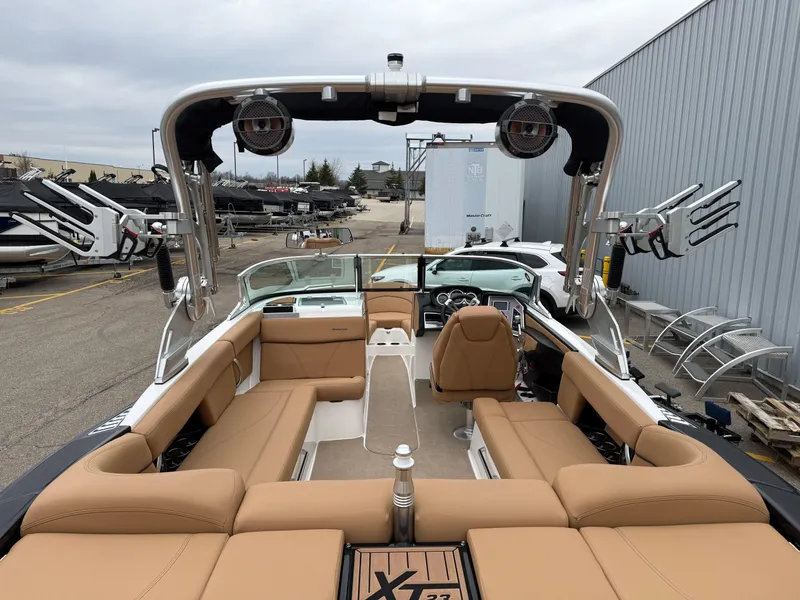 Slide: The Image of 2018 MasterCraft XT23 boat with tan seating and wakeboard racks, parked outdoors. - 7