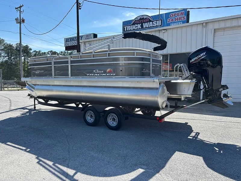 Slide: The Image of 2025 Sun Tracker Party Barge 20 DLX pontoon boat on trailer, parked outdoors. - 2