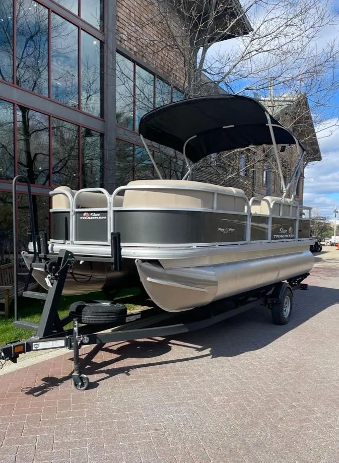 Slide: The Image of 2025 Sun Tracker Party Barge 18 DLX pontoon boat on trailer, parked outdoors. - 2