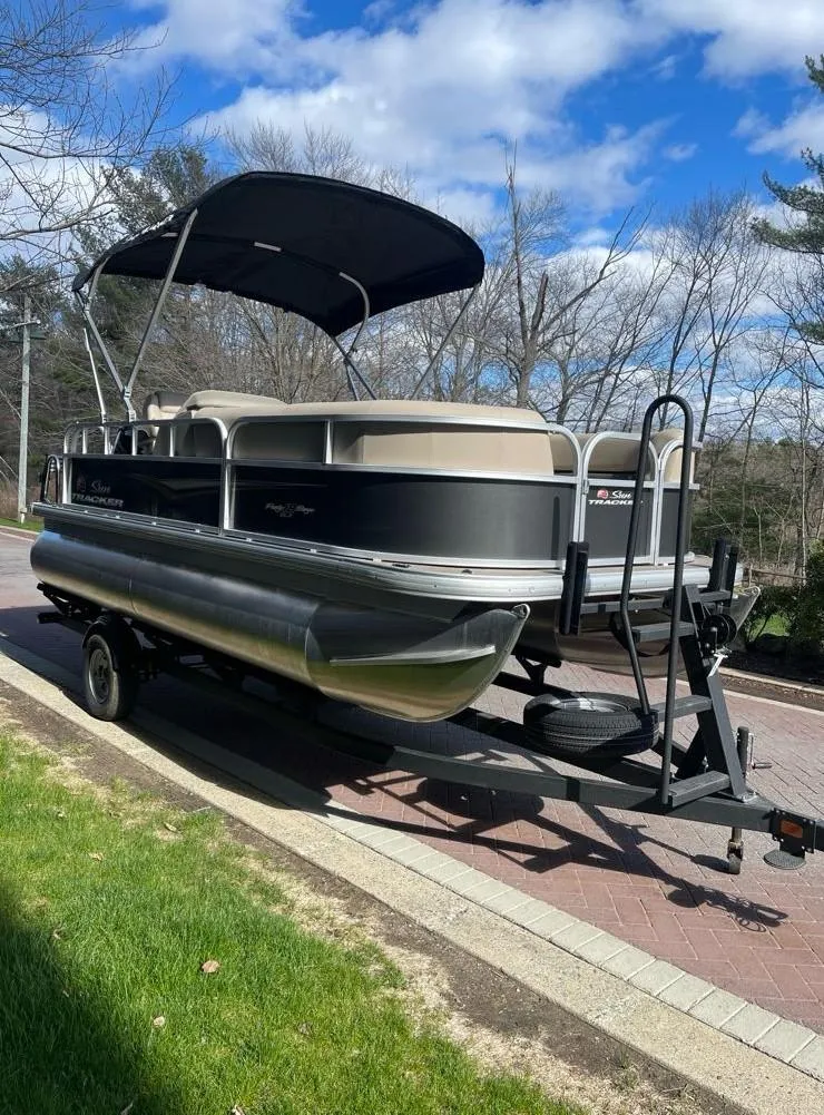 Slide: The Image of 2025 Sun Tracker Party Barge 18 DLX pontoon boat on trailer, parked outdoors. - 3