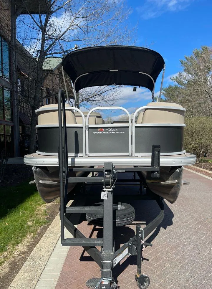 Slide: The Image of 2025 Sun Tracker Party Barge 18 DLX pontoon boat on trailer, parked outdoors. - 4