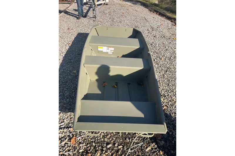 Slide: The Image of 2025 Tracker Grizzly 10 Jon boat on gravel, shadow visible inside. - 2