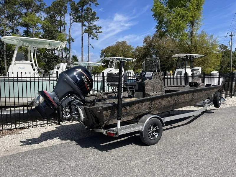 Slide: The Image of 2025 Xpress H210B boat on trailer, camo design, parked outdoors near other boats. - 2