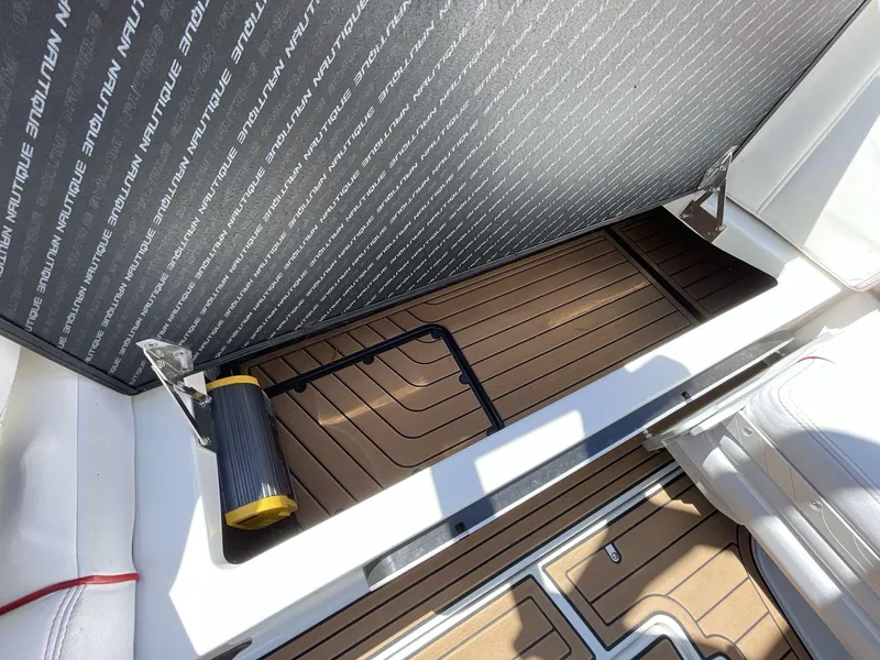 Slide: The Image of 2017 Nautique Super Air G23 storage compartment with brown flooring and a black handle. - 26