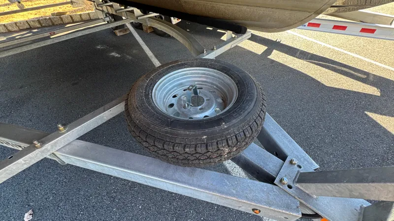 Slide: The Image of Trailer wheel on a 2003 Godfrey Sweet Water boat trailer, parked on asphalt. - 25