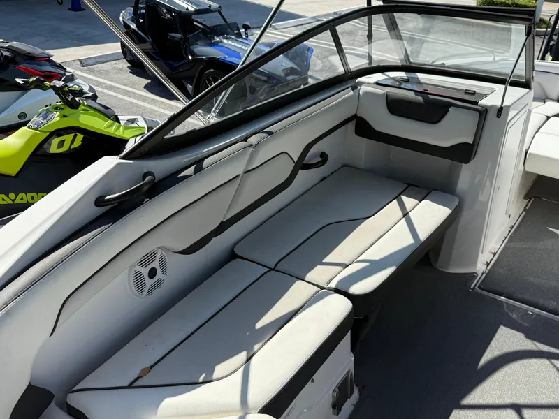 Slide: The Image of 2018 Yamaha Boats SX210 interior with seating and speaker, parked near jet skis. - 14