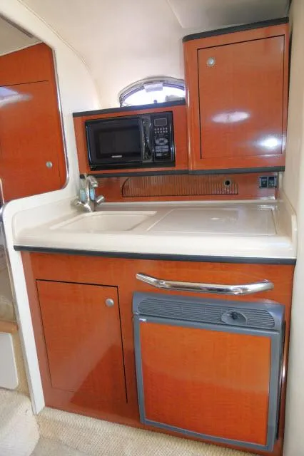Slide: The Image of 2005 Sea Ray 280 Sundancer galley with wood cabinetry, microwave, and compact fridge. - 10