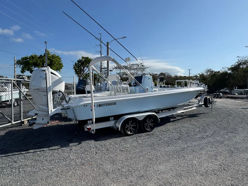 Slide: The Image of 2024 Contender 26 Bay boat on trailer, parked outdoors under clear blue sky. - 1