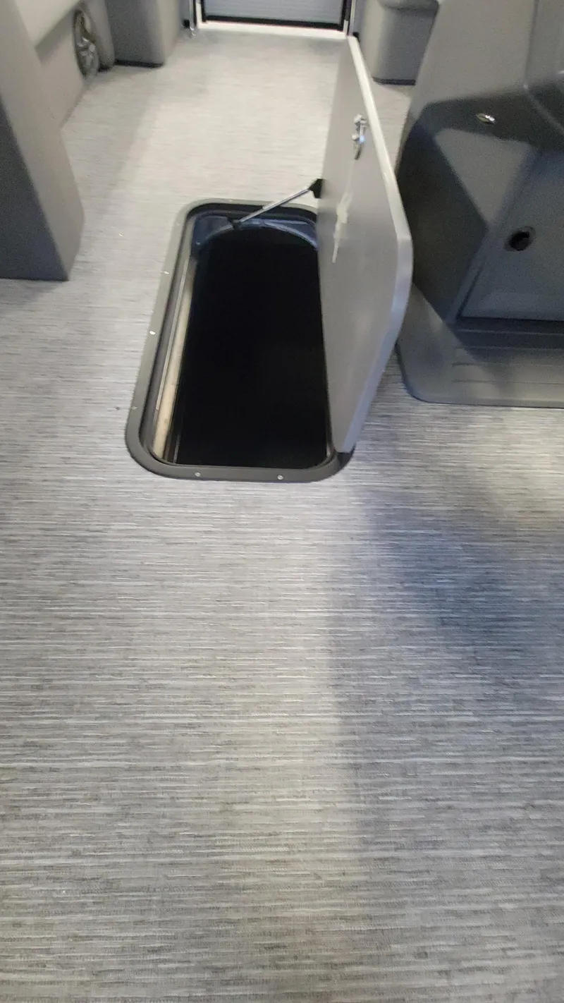 Slide: The Image of 2025 Qwest E22 interior with open floor storage compartment, gray carpeted flooring. - 13