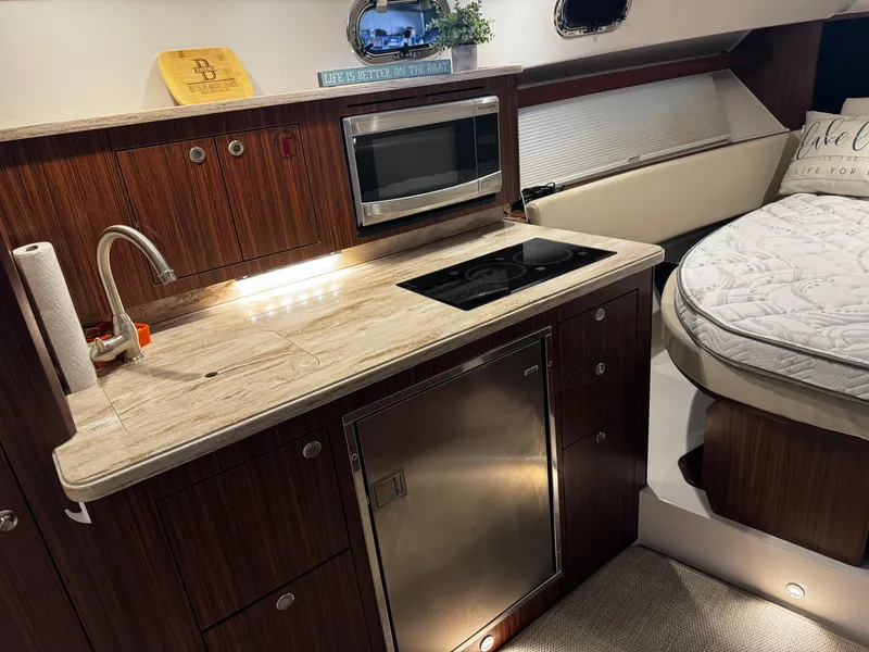 Slide: The Image of 2018 Pursuit OS 355 Offshore interior with kitchenette, featuring sink, stove, microwave, and cozy bed. - 28