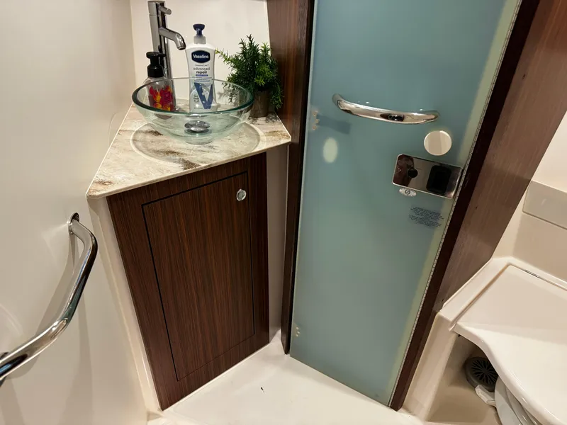 Slide: The Image of 2018 Pursuit OS 355 Offshore bathroom with glass sink, wooden cabinet, and frosted door. - 42