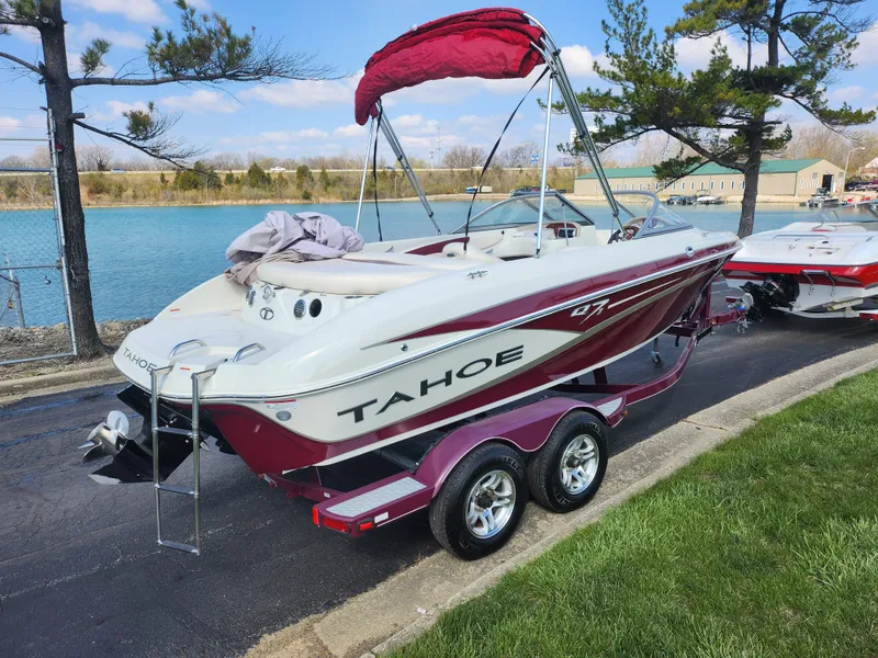 Slide: The Image of 2013 Tahoe Q7i boat on trailer by a lake, with red canopy and scenic background. - 1