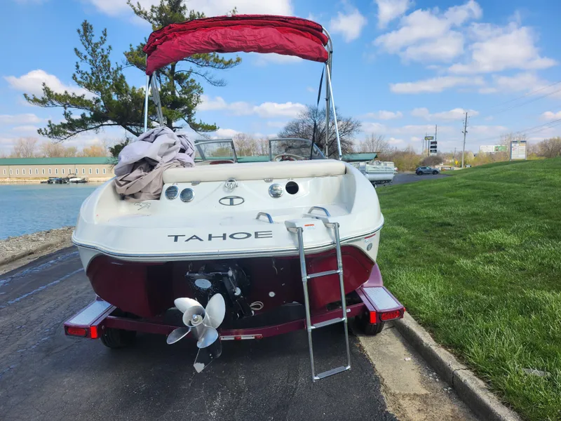 Slide: The Image of 2013 Tahoe Q7i boat with red canopy, parked near a lake under a blue sky. - 2